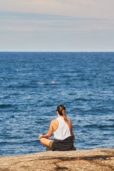 Serene scene of a woman meditating on a rocky shore with the ocean view.