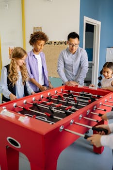 Teacher and students enjoying a foosball game in a school classroom during daytime.